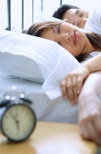 Couple sleeping on bed, alarm clock in foreground, selective focus - Asia Images Group