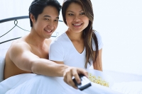 Couple sitting on bed, watching TV - Asia Images Group