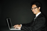 Businessman wearing glasses, with laptop, smiling at camera - Asia Images Group