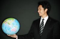 Businessman holding globe in one hand, smiling - Asia Images Group