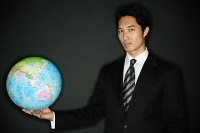 Businessman holding globe in one hand, looking at camera - Asia Images Group
