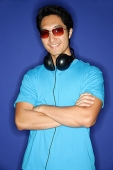 Man wearing sunglasses, headphones around his neck, arms crossed - Asia Images Group