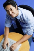 Man wearing headset, using laptop, smiling up at camera - Asia Images Group