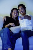 Couple sitting on sofa, watching TV, man pointing finger - Asia Images Group