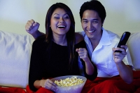 Couple watching TV, making fists, smiling - Asia Images Group