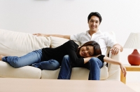 Couple on sofa, woman lying on mans lap, looking at camera - Asia Images Group