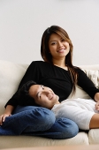 Couple on sofa, man lying on womans lap, both smiling at camera - Asia Images Group