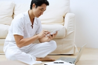 Man sitting on floor, using laptop and calculator - Asia Images Group