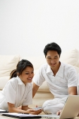 Couple at home in living room, looking at laptop - Asia Images Group