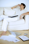 Man lying on sofa, sleeping, hand on head, laptop and documents on floor next to him - Asia Images Group