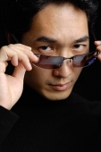 Man adjusting sunglasses, looking at camera - Asia Images Group