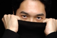 Man pulling turtleneck over face, looking at camera - Asia Images Group