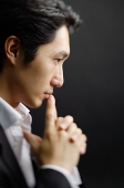 Man with clasped hands, fingers on mouth - Asia Images Group