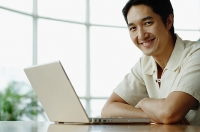 Man smiling at camera, laptop on table - Asia Images Group