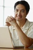 Man with laptop, leaning elbows on table, hands clasped - Asia Images Group