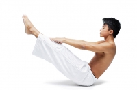 Man doing yoga, sitting on floor, raising leg - Asia Images Group