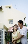 Couple standing in front of house, embracing - Asia Images Group