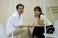 Couple sitting on swing, holding hands, looking at the camera - Asia Images Group
