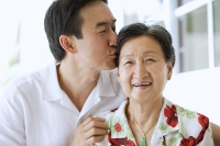 Mother and adult son together, son giving mother a kiss - Asia Images Group