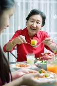 Grandmother and granddaughter at dining table, eating - Asia Images Group