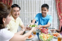 Mother and son passing food to each other at dining table - Asia Images Group