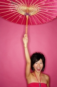 Woman holding pink umbrella, standing against pink background - Asia Images Group