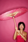 Woman holding pink umbrella, looking up - Asia Images Group