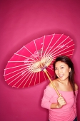 Woman holding umbrella, wearing pink top, standing against pink background - Asia Images Group