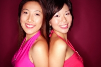 Two young women standing back to back, smiling at camera - Asia Images Group