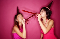 Young women wearing party hats, blowing noisemakers - Asia Images Group