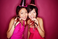 Young women wearing party hats, holding noisemakers, smiling at camera - Asia Images Group