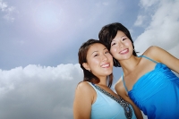 Two women standing cheek to cheek, smiling at camera, low angle view - Asia Images Group