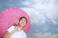 Young woman with pink umbrella, smiling, low angle view - Asia Images Group