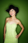 Woman in green dress, wearing cowboy hat and earrings, smiling at camera - Asia Images Group