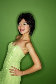 Woman in green dress, hands on hip, smiling at camera - Asia Images Group