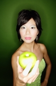 Woman in green dress, holding green apple towards camera - Asia Images Group