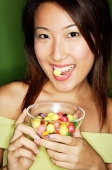 Woman eating candy and holding candy bowl - Asia Images Group