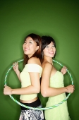 Two women standing back to back, hoola hoop around them - Asia Images Group