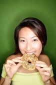 Woman biting into donut, looking at camera - Asia Images Group