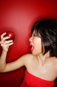 Woman in red tube tope holding red apple, mouth open - Asia Images Group