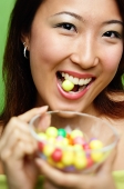 Woman biting candy and holding candy bowl - Asia Images Group