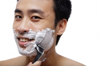 Man shaving face, looking at camera, smiling - Asia Images Group