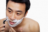 Man holding shaver to face, shaving - Asia Images Group