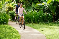 Young couple cycling through a park, smiling - Asia Images Group