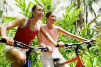 Two girls smiling and riding bikes through a park - Asia Images Group