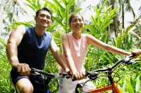 Man and Woman riding bikes through a park, smiling - Asia Images Group