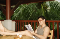Man sitting with feet up on table, reading - Asia Images Group