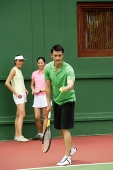 Man serving a game of tennis with two women watching - Asia Images Group