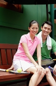 Portrait of Man and Woman sitting on bench with tennis racket, looking at camera and smiling - Asia Images Group