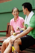 Couple sitting on bench in tennis court, looking at each other - Asia Images Group